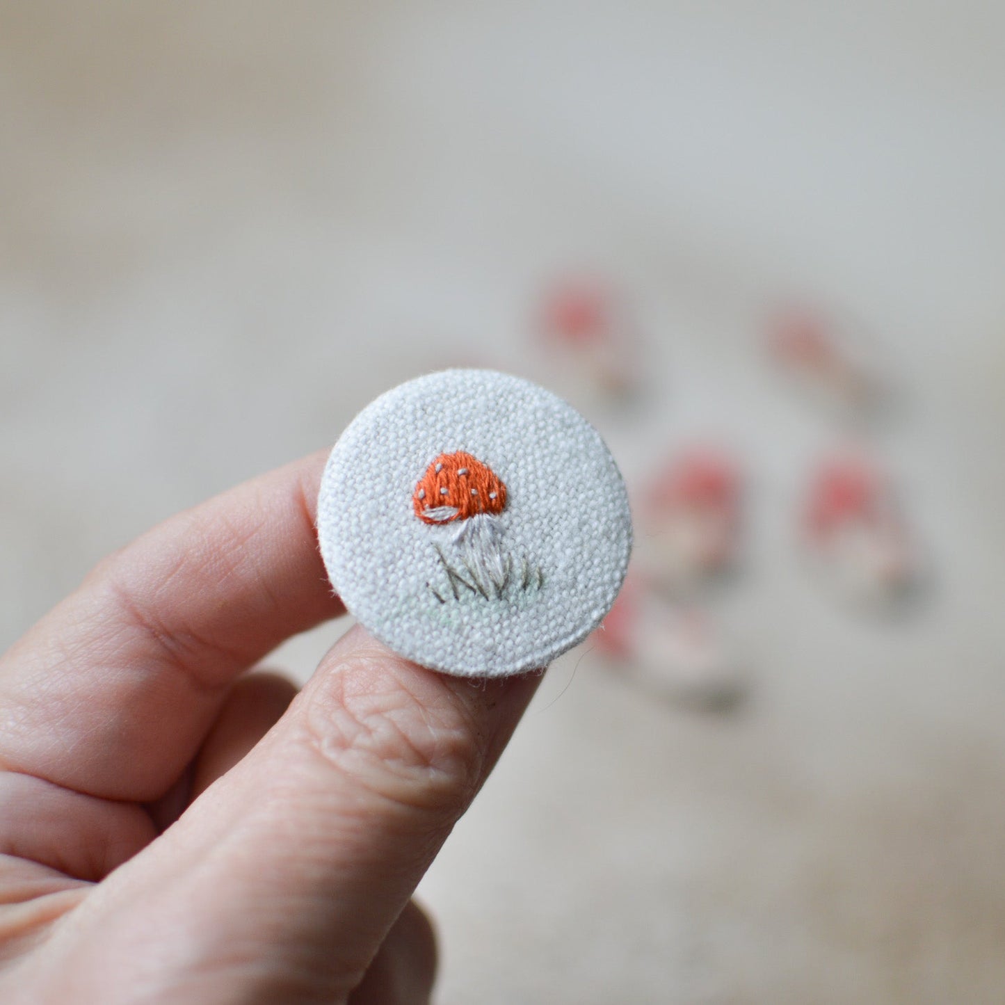 Circular embroidered patch with a mushroom design held by a hand against a blurred background