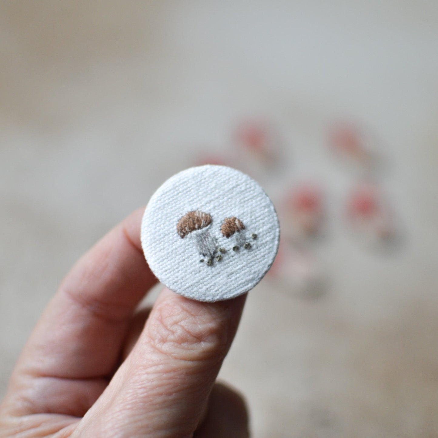 Circular embroidered patch withmushroomsheld by a hand against a blurred background