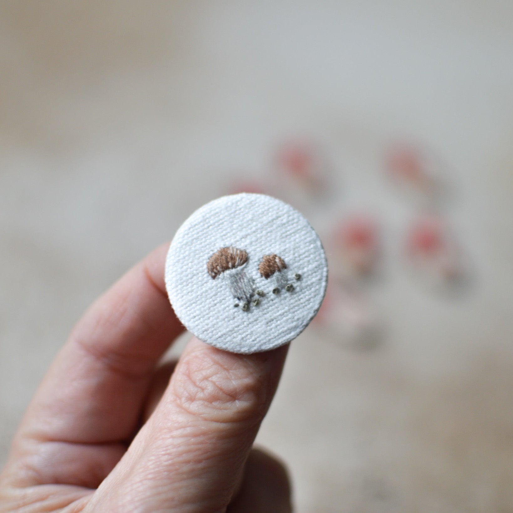 Circular embroidered patch withmushroomsheld by a hand against a blurred background